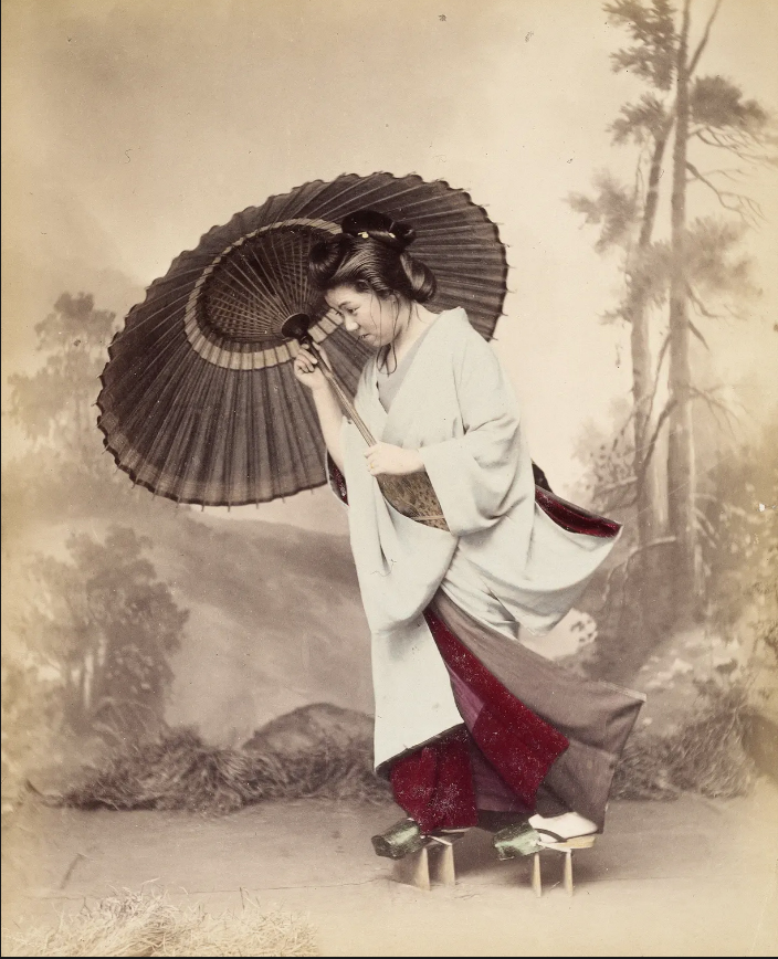 Без названия (женщина с зонтиком), 1880-е

В 1880-х в Токио, Киото и Иокогаме было множество фотостудий, создающих фотографии, нередко рассчитанные на европейскую аудиторию. Эти альбомы фотографий обычно включали красивые, живописные пейзажи и студийные портреты японцев, занятых обычными делами. Эта фотография изображает женщину, идущую в штормовую, ветреную погоду – но снята она в студии, с рисованным задником. Она склоняется против ветра, и её кимоно хлопает, как парус – но, присмотревшись внимательно, можно увидеть оттягивающие его нити. Это совершенно фантастический образ. Фотограф - неизвестен